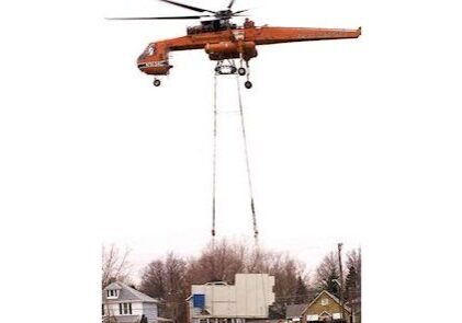 A crane is lifting a helicopter over a house.